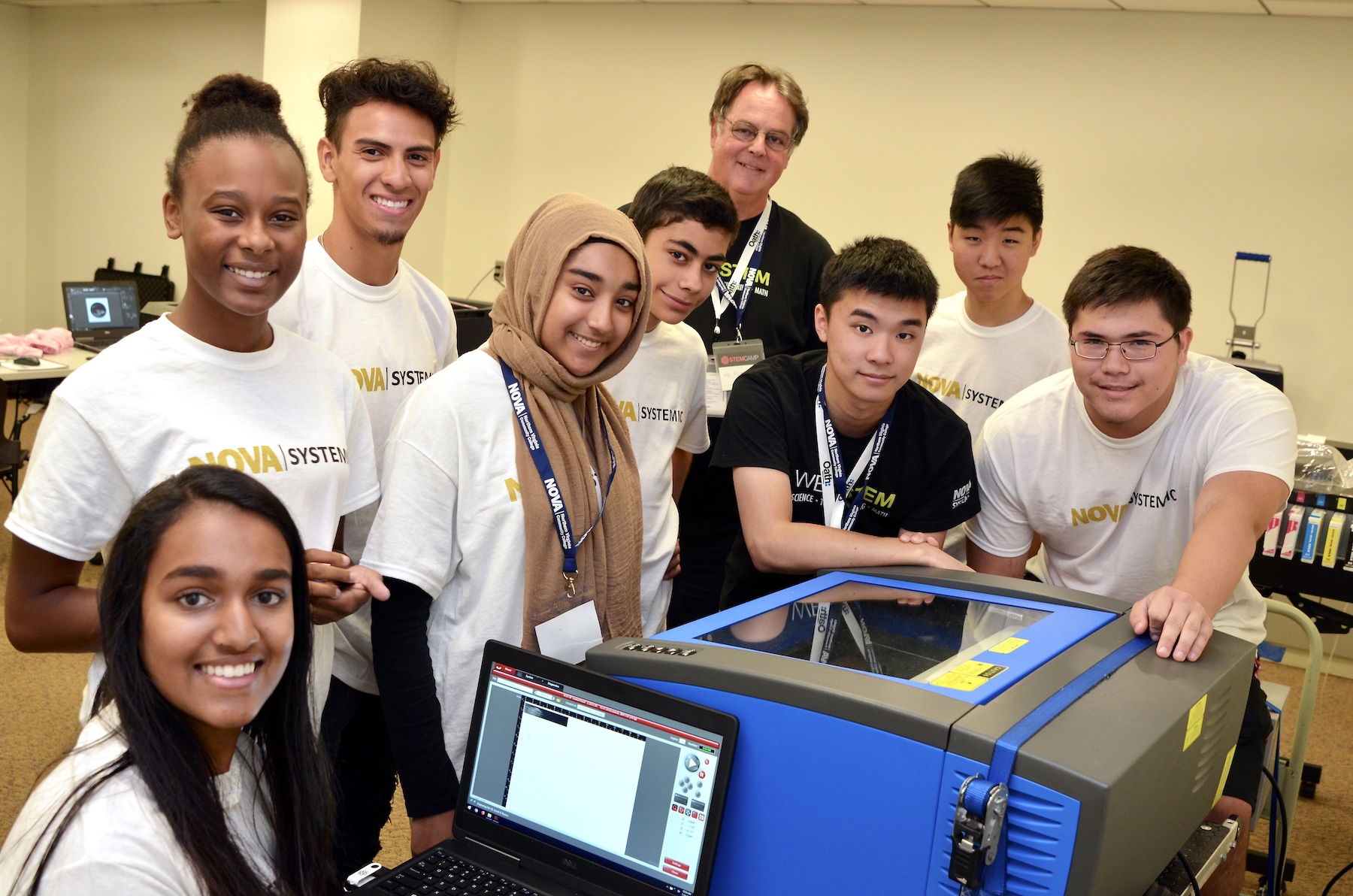 A group of students standing around a computer and a 3D printer, smiling