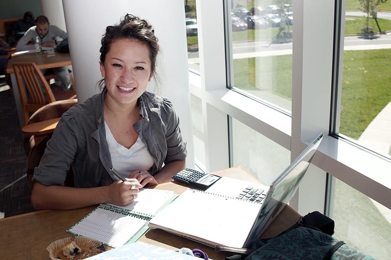 A student sitting at a table with her laptop and notebook, smiling.