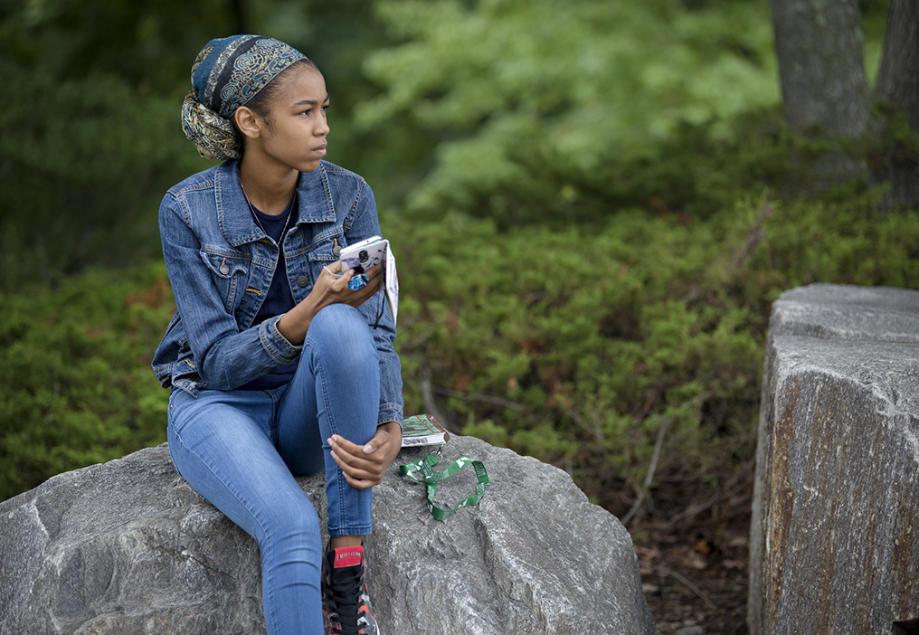 student sitting on a rock holding her mobile phone